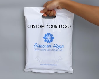 Op de afbeelding: Witte plastic boodschappentas met een gestanste handgreep, met bovenaan de tekst "CUSTOM YOUR LOGO". Daaronder een blauw bloemenlogo en de woorden "Discover Hope Behavioral Solutions, Inc."