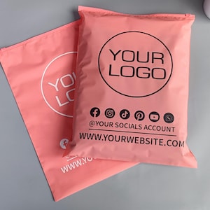 May include: Two pink mailer bags with black and white text. The larger bag has a circular logo that says "YOUR LOGO" and social media icons below. The smaller bag has a similar logo. The website address is also visible.
