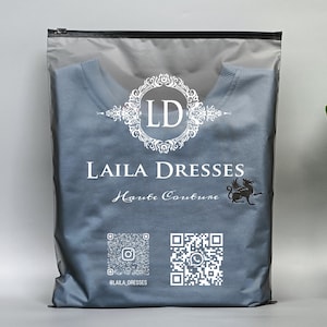 May include: A gray plastic bag with a black zipper, containing a blue shirt. The bag features the text "LAILA DRESSES Haute Couture" in white, along with a logo and QR codes for social media.