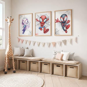 May include: Three framed wall art prints featuring cartoon superhero characters in red, blue, and purple suits with spider web motifs. The prints are displayed above a long wooden storage bench with beige fabric bins and plush cushions.