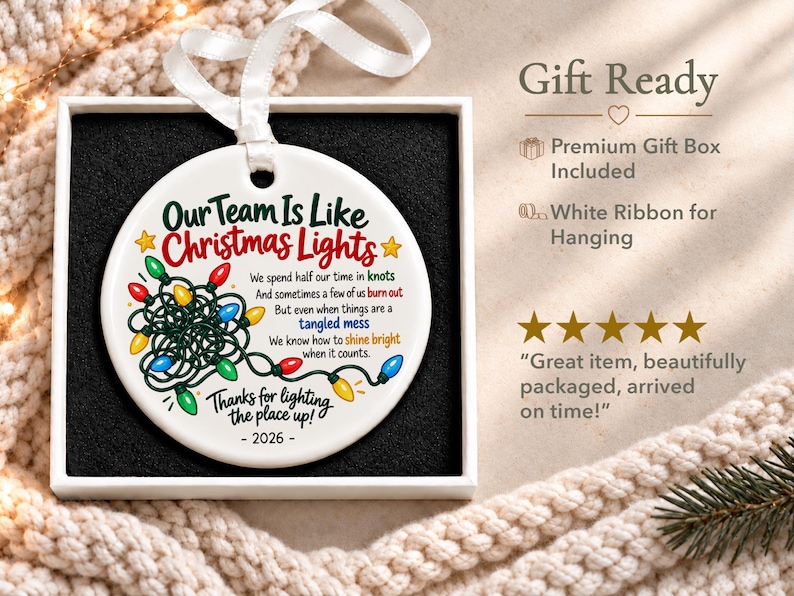 May include: A round white ceramic ornament with a white ribbon, featuring a graphic of tangled multi-coloured Christmas lights and the text: Our Team Is Like Christmas Lights, We spend half our time in knots, And sometimes a few of us burn out, But even when things are a tangled mess, We know how to shine bright when it counts, Thanks for lighting the place up, - 2026 -.