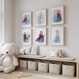 Puede incluir: Seis láminas de arte enmarcadas con ilustraciones en acuarela de los personajes de la película Frozen, incluyendo a Anna, Elsa, Olaf y Kristoff con Sven, dispuestas en dos filas sobre un banco de madera con cajas de almacenamiento.