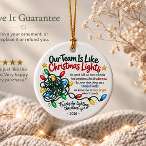 May include: A round white ceramic ornament hanging by a gold cord. It features a graphic of tangled multi-coloured Christmas lights and text that reads: Our Team Is Like Christmas Lights, We spend half our time in knots, And sometimes a few of us burn out, But even when things are a tangled mess, We know how to shine bright when it counts, Thanks for lighting the place up! - 2026 -