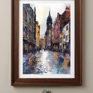 May include: A framed watercolor print depicting a narrow European cobblestone street lined with multi-story buildings in shades of yellow, red, and grey. A tall clock tower stands in the distance under a bright sky, with reflections on the wet ground.