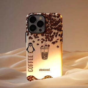 May include: A phone case with a coffee theme. The case features a penguin, a coffee cup, and coffee beans. The word "coffee" is printed vertically, and the word "obsessed" is printed horizontally. The case is set against a cream-coloured background.