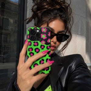 May include: A smartphone case featuring a vibrant neon green background with a repeating black and hot pink leopard print pattern. The case has a precise cutout for the camera lens array, showcasing a textured finish across the entire surface.
