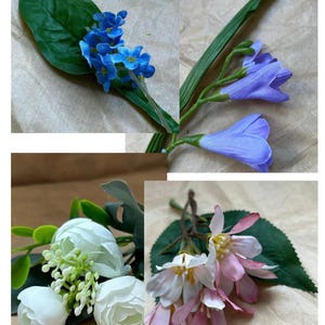 May include: A collection of artificial floral stems featuring small blue flowers with green leaves, purple bell-shaped blossoms, white rounded flower buds with green foliage, and pink and white star-shaped flowers with green leaves.