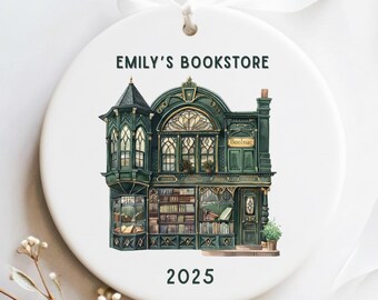 May include: A white ceramic Christmas ornament with a detailed illustration of a green bookstore. The text "Emily's Bookstore" and the year "2025" are displayed. It has a white ribbon for hanging.