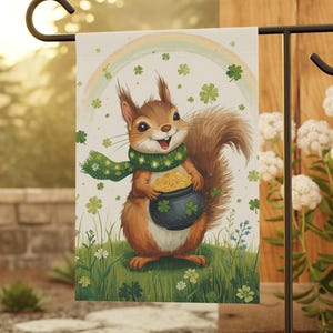 May include: A garden flag featuring a cartoon squirrel holding a pot of gold. The squirrel wears a green scarf and stands on a grassy hill with shamrocks and a rainbow in the background. The flag is mounted on a black metal stand.
