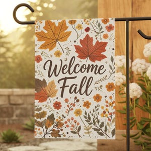 May include: A rectangular garden flag featuring a white background with a pattern of autumn leaves, small flowers, and berries in shades of orange, red, and brown. The text "Welcome Fall" is printed in a dark brown script font in the center.