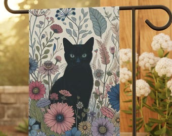Puede incluir: Una bandera de jardín con un gato negro en medio de un colorido arreglo floral. El gato tiene ojos azules y está rodeado de flores rosas, azules y moradas. El fondo es de color crema con patrones florales y de hojas.