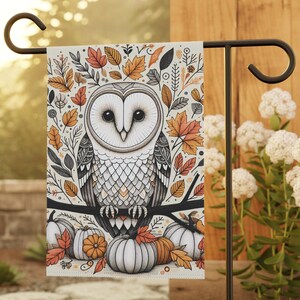 May include: A rectangular garden flag featuring a central illustration of a barn owl perched on a branch. The design includes orange and brown autumn leaves, pumpkins, and intricate line work. The flag hangs from a black metal garden stake.