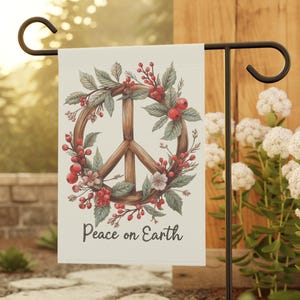 May include: A garden flag featuring a peace symbol made of wood, surrounded by a wreath of leaves, berries, and flowers. The flag has the words "Peace on Earth" printed on it. The flag is displayed on a black metal stand.