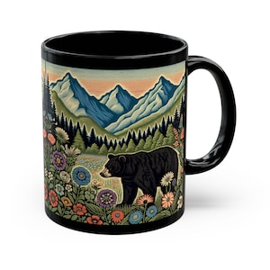 May include: Black ceramic mug featuring a nature scene with a black bear, mountains, and colorful flowers. The design wraps around the mug, showcasing a detailed illustration of a forest landscape.