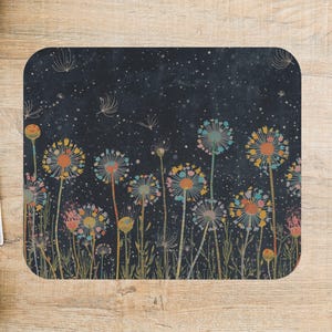 May include: A square coaster with a dark blue background featuring a colorful dandelion design. The dandelions have orange, blue, and pink flower heads with delicate seed heads floating above. The coaster is on a wooden surface.