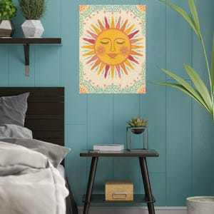 May include: A decorative wall art print featuring a smiling sun with closed eyes. The sun has yellow, orange, and red rays, set against a cream background with a decorative border. The artwork is displayed on a teal wall.