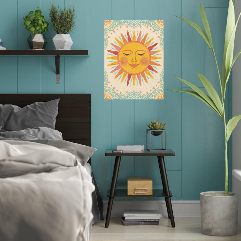 May include: A decorative wall art print featuring a smiling sun with closed eyes. The sun has yellow, orange, and red rays, set against a cream background with a decorative border. The artwork is displayed on a teal wall.