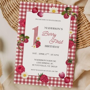 Puede incluir: Una invitación de cumpleaños con un borde de cuadros rojos y blancos, adornada con ilustraciones de frambuesas y margaritas. La invitación dice "MADDISON'S Berry First BIRTHDAY" con detalles del evento. Fondo blanco.