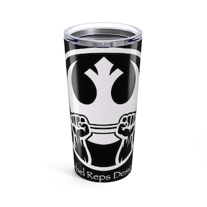 Puede incluir: Un vaso negro y blanco con un diseño gráfico blanco y dos puños sosteniendo una barra. El texto "Rebel Reps Design" está impreso en la parte inferior. El vaso tiene una tapa transparente. Mide aproximadamente 18 cm de alto.