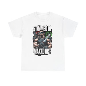 May include: White t-shirt featuring a muscular figure with sunglasses, holding a weapon and a syringe. The text "STIMMED UP" and "MAXED OUT" are printed above and below the figure in a bold, black font. The design has a comic book style.