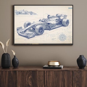 May include: Framed blueprint-style print of a Formula 1 race car. The artwork features detailed technical drawings in blue on a cream background, with the word "Ferrari" visible. The print is displayed in a black frame.