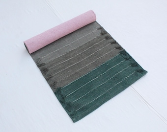 Op de afbeelding: Een opgerolde yogamat met een kleurengradatie van roze naar groen. De mat heeft een geweven textuur met witte horizontale strepen en franjes aan het uiteinde. De mat is ontworpen voor yoga en beweging.