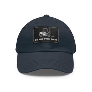 May include: Navy blue baseball cap with a rectangular patch featuring a forklift graphic and the text "DO YOU EVEN LIFT?". The cap has a curved brim and a structured crown.