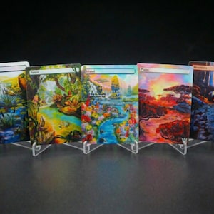 Könnte beinhalten: Fünf Landschaftskunstkarten, jeweils auf einem transparenten Ständer ausgestellt. Die Karten zeigen lebendige Szenen mit den Titeln "Swamp", "Forest", "Island", "Plains" und "Mountain". Die Kunstwerke zeigen farbenfrohe Naturumgebungen.