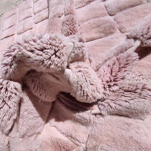 May include: Close-up of a plush, pink faux fur blanket. The blanket has a quilted design with a soft, textured surface. The folds and layers create depth and dimension, highlighting the luxurious feel of the material.