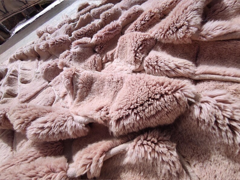 May include: Close-up of a plush, textured blanket in a muted rose color. The blanket features a layered design with raised, fluffy sections, creating a soft, inviting appearance. The overall aesthetic suggests comfort and warmth.