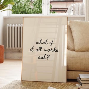 以下が含まれることがあります： ライトベージュの背景に黒の手書き風テキスト「what if it all works out?」が中央に配置された、長方形の額入りウォールアート。フレームは細い金属製で、プリントをすっきりとシンプルな形で囲んでいます。