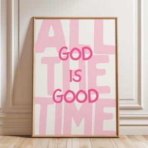 May include: A rectangular framed wall art print featuring the text ALL THE TIME GOD IS GOOD in bold, dark pink lettering. The background consists of large, light pink block letters spelling out the same phrase, set against a cream-colored backdrop.