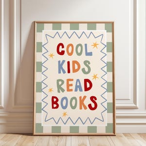 Puede incluir: Un cuadro decorativo rectangular con marco de madera que presenta un centro color crema con el texto COOL KIDS READ BOOKS en letras multicolores de estilo dibujado a mano, rodeado por un borde en zigzag azul y un patrón de cuadros verde salvia y crema.
