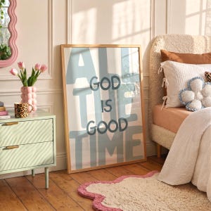 Pu&ograve; includere: Una stampa artistica da parete rettangolare incorniciata con il testo "GOD IS GOOD ALL THE TIME" in lettere blu scuro, in grassetto e arrotondate su uno sfondo azzurro. La stampa &egrave; inserita in una cornice di legno chiaro appoggiata a una parete.