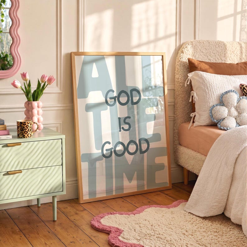 Pu&ograve; includere: Una stampa artistica da parete rettangolare incorniciata con il testo "GOD IS GOOD ALL THE TIME" in lettere blu scuro, in grassetto e arrotondate su uno sfondo azzurro. La stampa &egrave; inserita in una cornice di legno chiaro appoggiata a una parete.