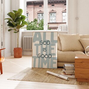 Pu&ograve; includere: Una stampa da parete rettangolare incorniciata con uno sfondo beige chiaro e grandi lettere a blocchi blu tenue che compongono la frase ALL THE TIME, con un testo pi&ugrave; piccolo in grigio scuro centrato che recita GOD IS GOOD.