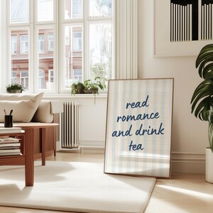 May include: A rectangular framed wall art print featuring a light blue and white vertical striped background with the dark blue text "read romance and drink tea" centered in a casual, handwritten-style font within a thin wooden frame.