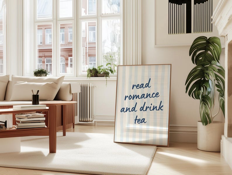 May include: A rectangular framed wall art print featuring a light blue and white vertical striped background with the dark blue text "read romance and drink tea" centered in a casual, handwritten-style font within a thin wooden frame.