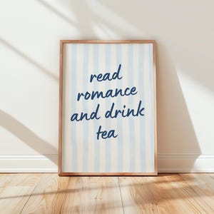 May include: A rectangular framed wall art print featuring vertical light blue stripes on a white background. The text "read romance and drink tea" is printed in a dark blue, handwritten-style font centered on the print within a wooden frame.