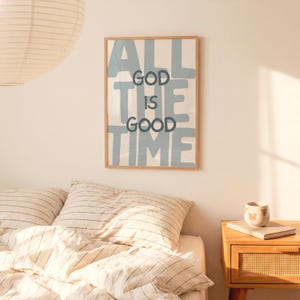 Pu&ograve; includere: Una stampa artistica da parete rettangolare in una cornice di legno chiaro con il testo ALL GOD IS GOOD TIME in lettere blu scuro sovrapposte a grandi lettere in stampatello blu chiaro su sfondo bianco. La stampa &egrave; su una parete liscia.