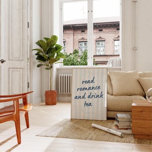 May include: A rectangular framed wall art piece featuring a light blue and white vertical striped background with the dark blue text read romance and drink tea centered on the surface. The print is displayed in a simple wooden frame.