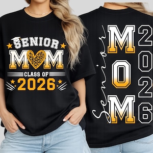 Puede incluir: Camiseta negra con "SENIOR MOM CLASS OF 2026" en letras blancas y doradas. El diseño incluye un gorro de graduación, estrellas y un estampado de leopardo en forma de corazón. La parte trasera de la camiseta dice "Senior Mom 2026".