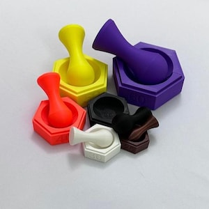 May include: A selection of brightly coloured weights and pestles. The weights are hexagonal and come in yellow, red, purple, black, white, and brown. Each weight has a number printed on it, indicating its weight in grams.