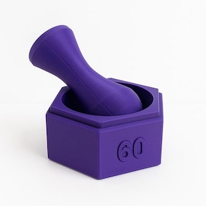 May include: A purple mortar and pestle set. The mortar is a hexagonal box with the number "60" embossed on one side. The pestle is a long, curved shape that fits inside the mortar. The set is made of a solid, matte material.