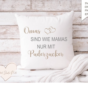 May include: A white square pillow with the German text "Omas sind wie Mamas nur mit Puderzucker" in a light brown script. Two heart shapes are above the word "Mamas". A white blanket is draped on the bottom right.