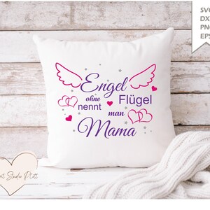 Puede incluir: Cojín cuadrado blanco con el texto "Engel ohne Flügel nennt man Mama" en morado y rosa. El diseño incluye alas de ángel, corazones y estrellas. Una manta de punto blanca y acogedora está drapeada debajo.