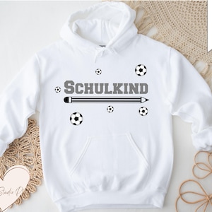 Puede incluir: Sudadera con capucha blanca con la palabra "SCHULKIND" en gris, un diseño de lápiz y diseños de balones de fútbol. El diseño está centrado en la parte delantera. Formatos de archivo disponibles: SVG, DXF, PNG y EPS.