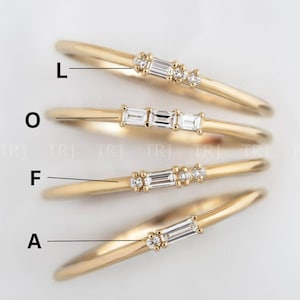 Könnte beinhalten: Vier zarte Goldringe mit kleinen, funkelnden Edelsteinen. Jeder Ring hat eine andere Anordnung der Steine, darunter Baguette- und Rundschliffe. Die Ringe werden auf einer weißen Oberfläche präsentiert, die ihr elegantes Design zeigt.