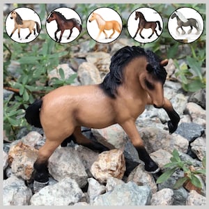 Op de afbeelding: Een bruin paardenbeeldje met een zwarte manen en staart staat op een bed van rotsen. Het paard staat in een dynamische houding, met één been omhoog. Verschillende kleinere paardenbeeldjes in verschillende kleuren staan op de achtergrond.