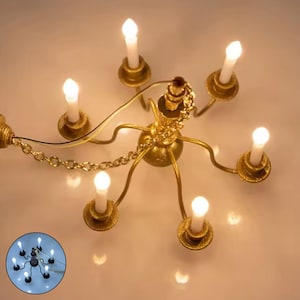 May include: A miniature gold-colored chandelier with seven candle-shaped lights. The chandelier has a detailed design with a chain and wiring. The lights are white and emit a soft glow, creating a warm ambiance. This decorative lighting fixture is ideal for dollhouses or miniature settings.